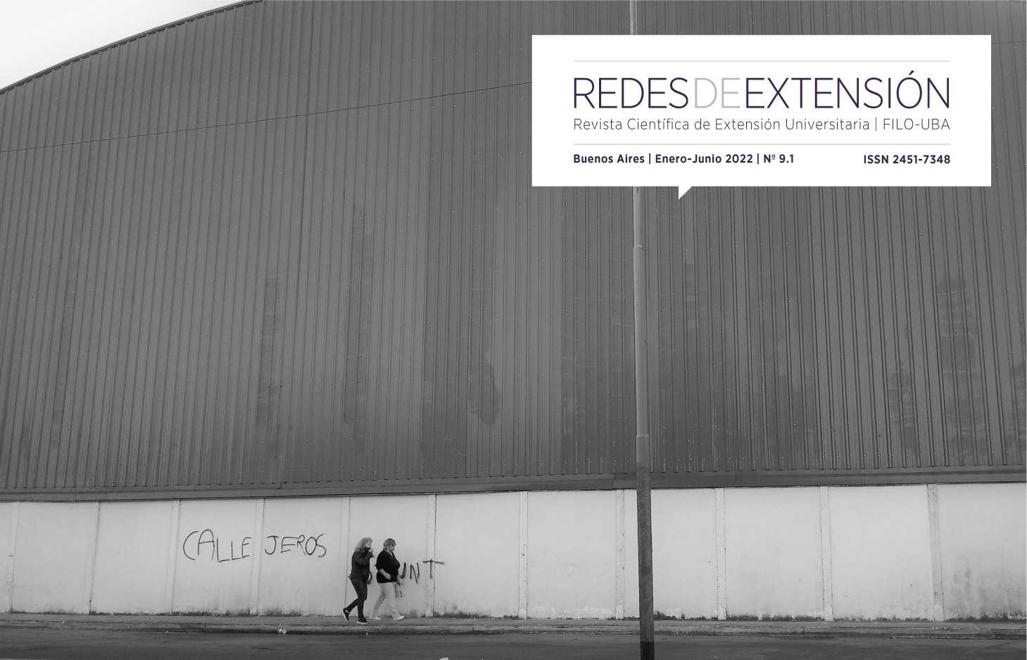 Fotografía en blanco y negro, dos mujeres caminan detrás una inmensa pared fabril